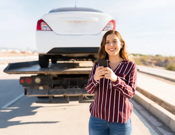 Mujer sonriente con un móvil en sus manos y una grúa con un coche de fondo