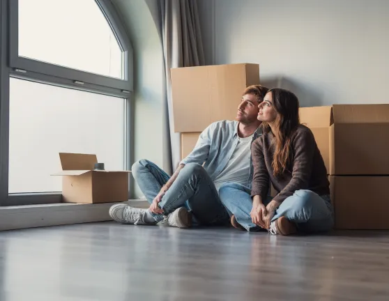 Pareja rodeada de cajas y sentada en el suelo mirando por la ventana