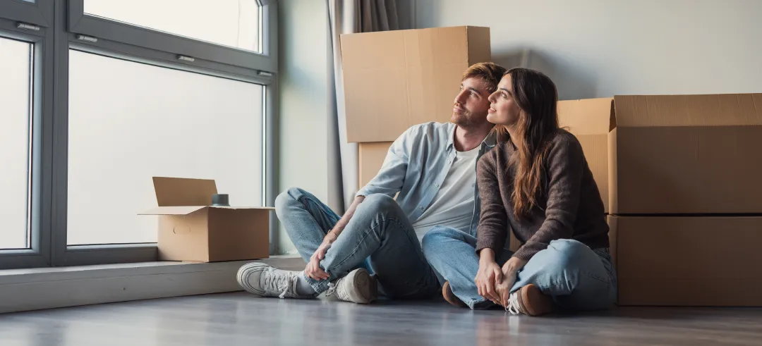 Pareja rodeada de cajas y sentada en el suelo mirando por la ventana