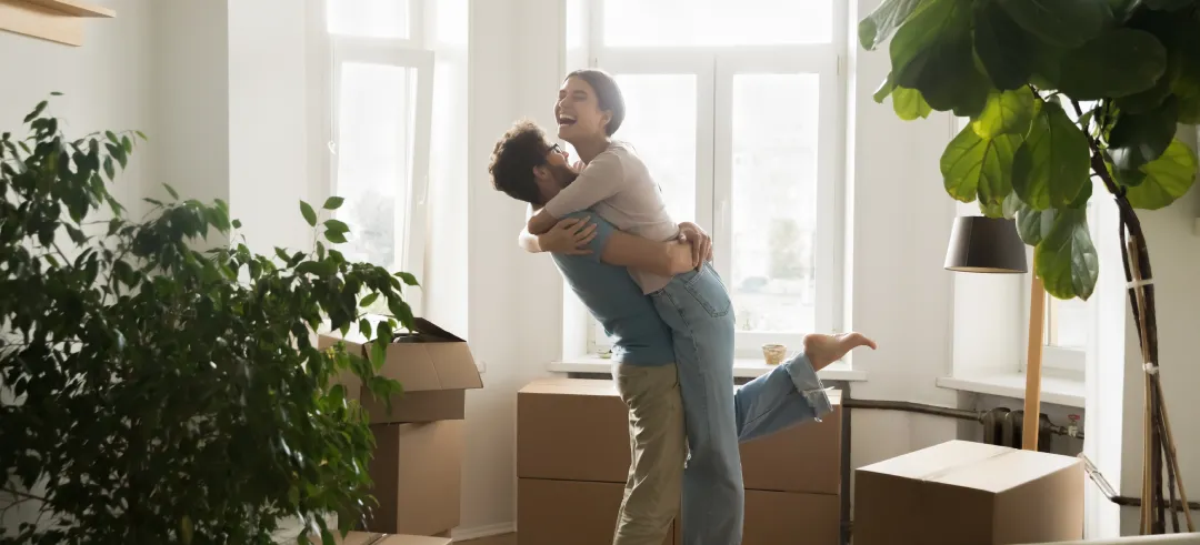 Pareja abrazándose y sonriendo en casa con mudanza