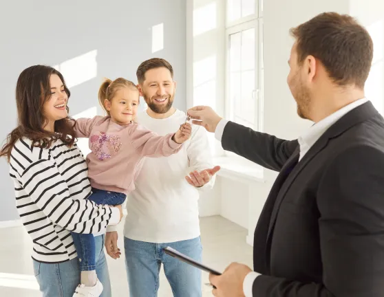 Niña en brazos de su madre cogiendo las llaves de una casa con su padre al lado