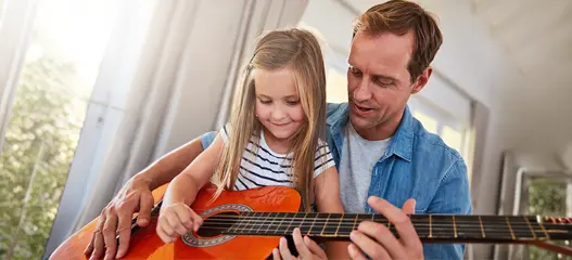 padre enseñando a hija a tocar la guitarra